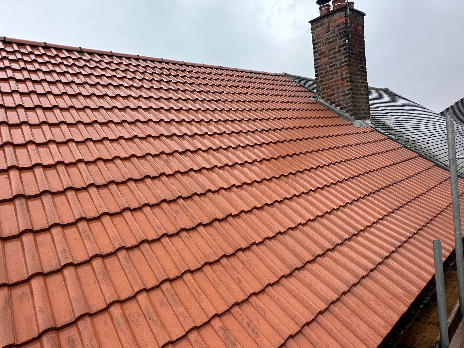 New terracotta red tiled roof finished next to a repointed brick chimney stack