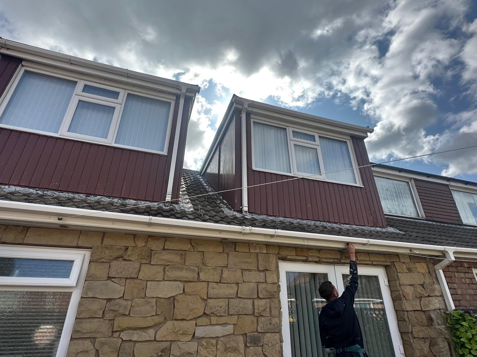 Roofer on a ladder installing white UPVC guttering and fascia boards on a residential dormer