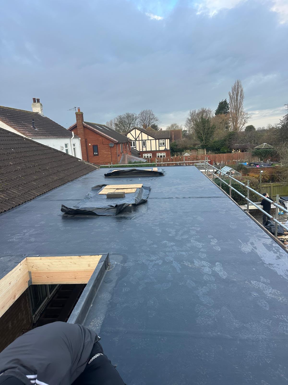 Black EPDM rubber membrane being laid across a large flat roof with scaffolding erected