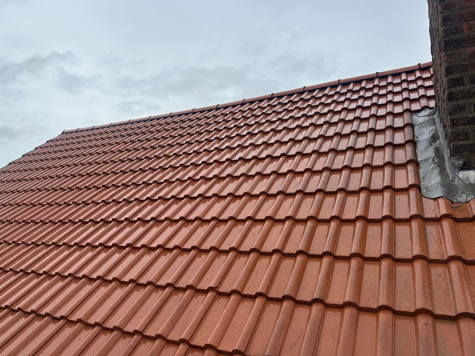 Fresh code-5 lead flashing dressed around a brick chimney on a new red tiled roof