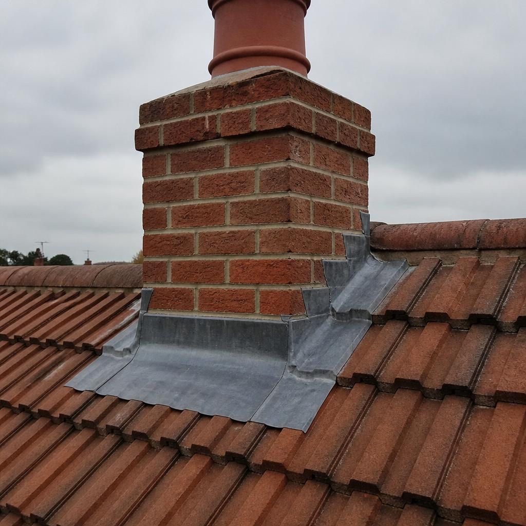 Close-up of a repointed red brick chimney stack with new grey lead flashing dressed neatly around the base on a red pantiled Yorkshire roof