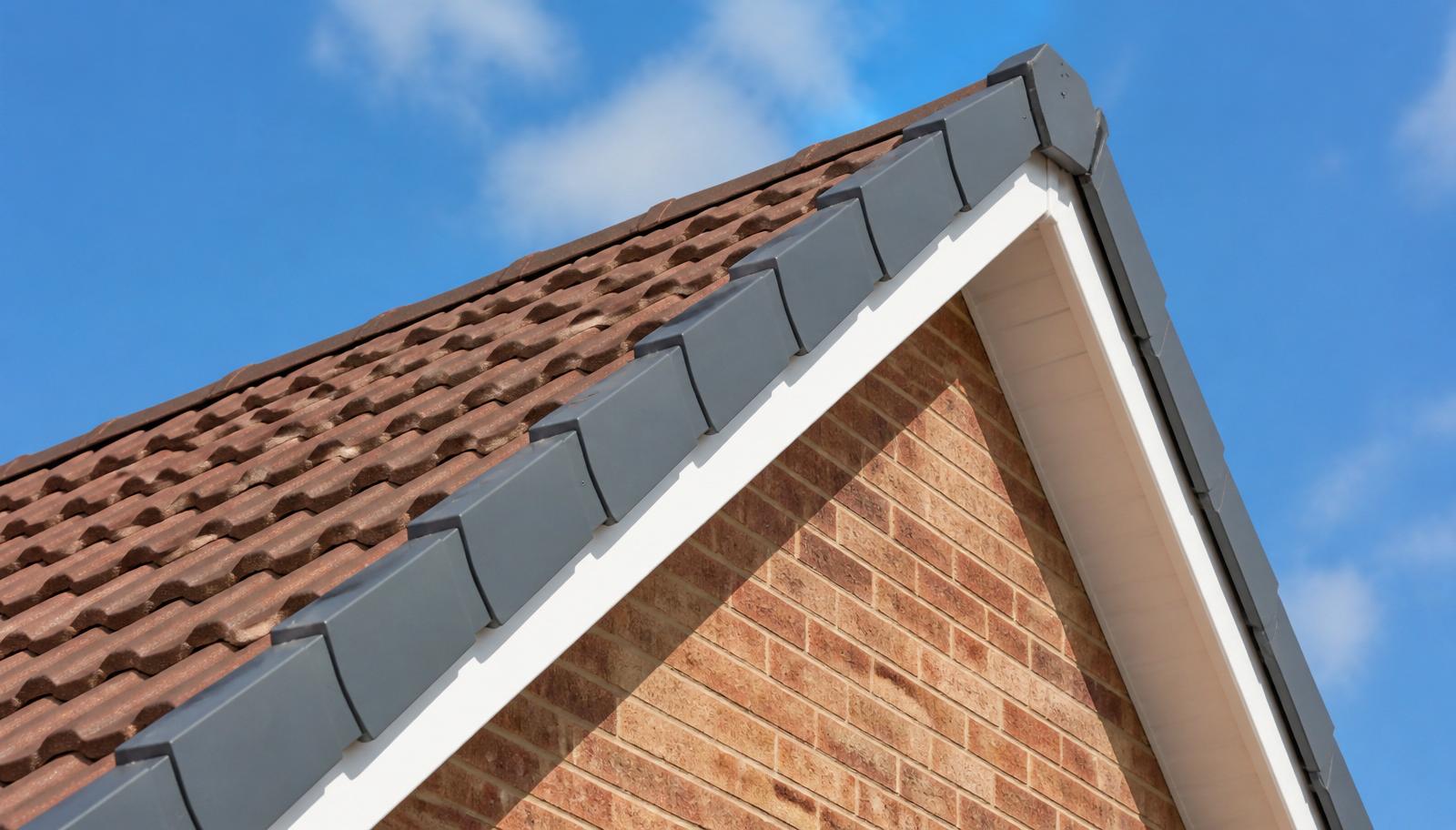 Close-up of a mechanically-fixed grey dry verge system running down the gable edge of a tiled roof over white UPVC fascia